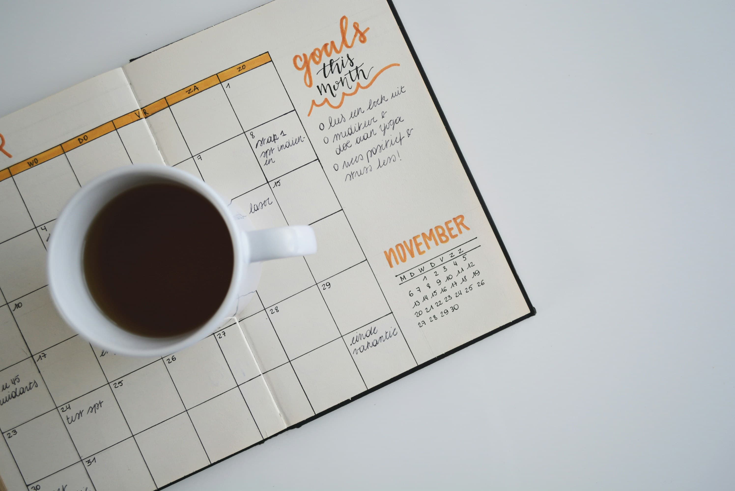 Foto de uma xícara de café em cima de uma agenda aberta sobre a mesa